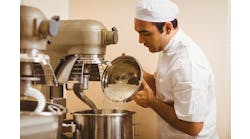 Baker-pouring-flour-into-large-mixer-in-a-commercial-kitchen