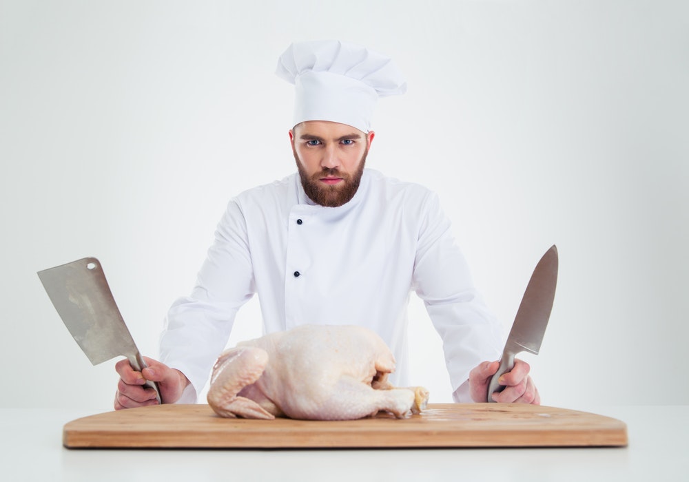 1661880597946 Portraitofaseriousmalechefcookstandingwithknifesandchickenonthetableisolate