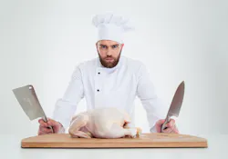 1661880597946 Portraitofaseriousmalechefcookstandingwithknifesandchickenonthetableisolate