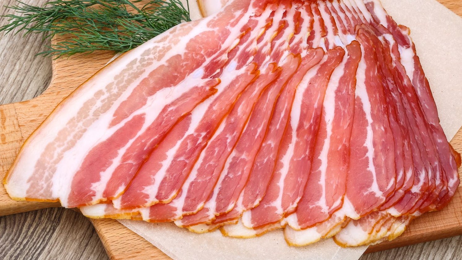 Fresh cold sliced bacon with dill branch on the wood background