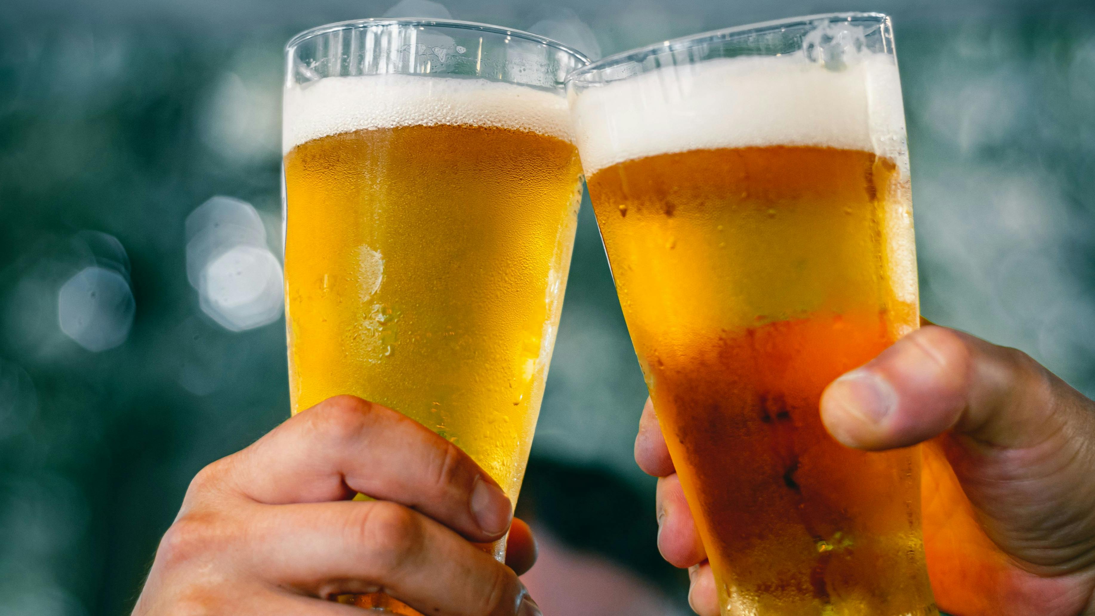Close-up view of a two glass of beer in hand. Beer glasses clinking at outdoor bar or pub