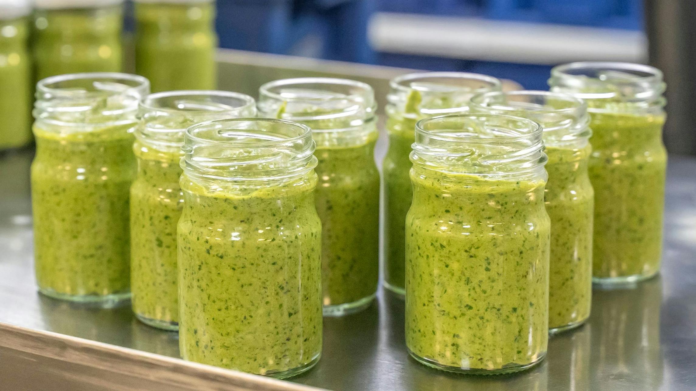 Pesto sauce Industrial process. High quality sauce production. Green pesto sauce in open jars on a food factory table. Italian basil taste in Pesto sauce