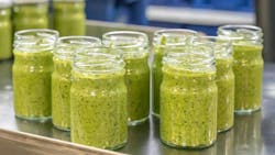 Pesto sauce Industrial process. High quality sauce production. Green pesto sauce in open jars on a food factory table. Italian basil taste in Pesto sauce Pesto sauce Industrial process. High quality sauce production. Green pesto sauce in open jars on a food factory table. Italian basil taste in Pesto sauce