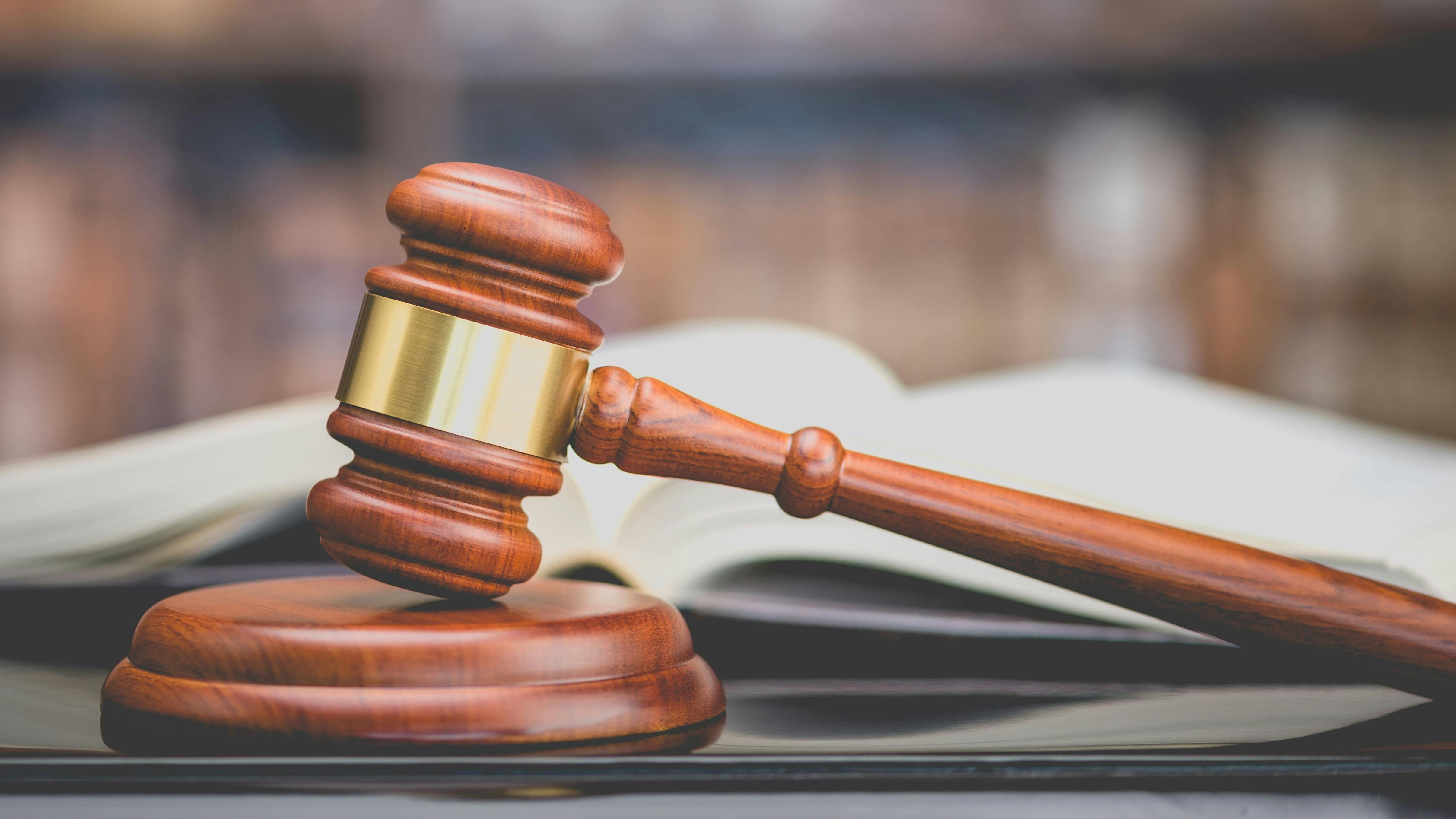 Judge's gavel or hammer and base used by a judge person on a desk in a courtroom with blurred books and a bookshelf or bookcase in the background