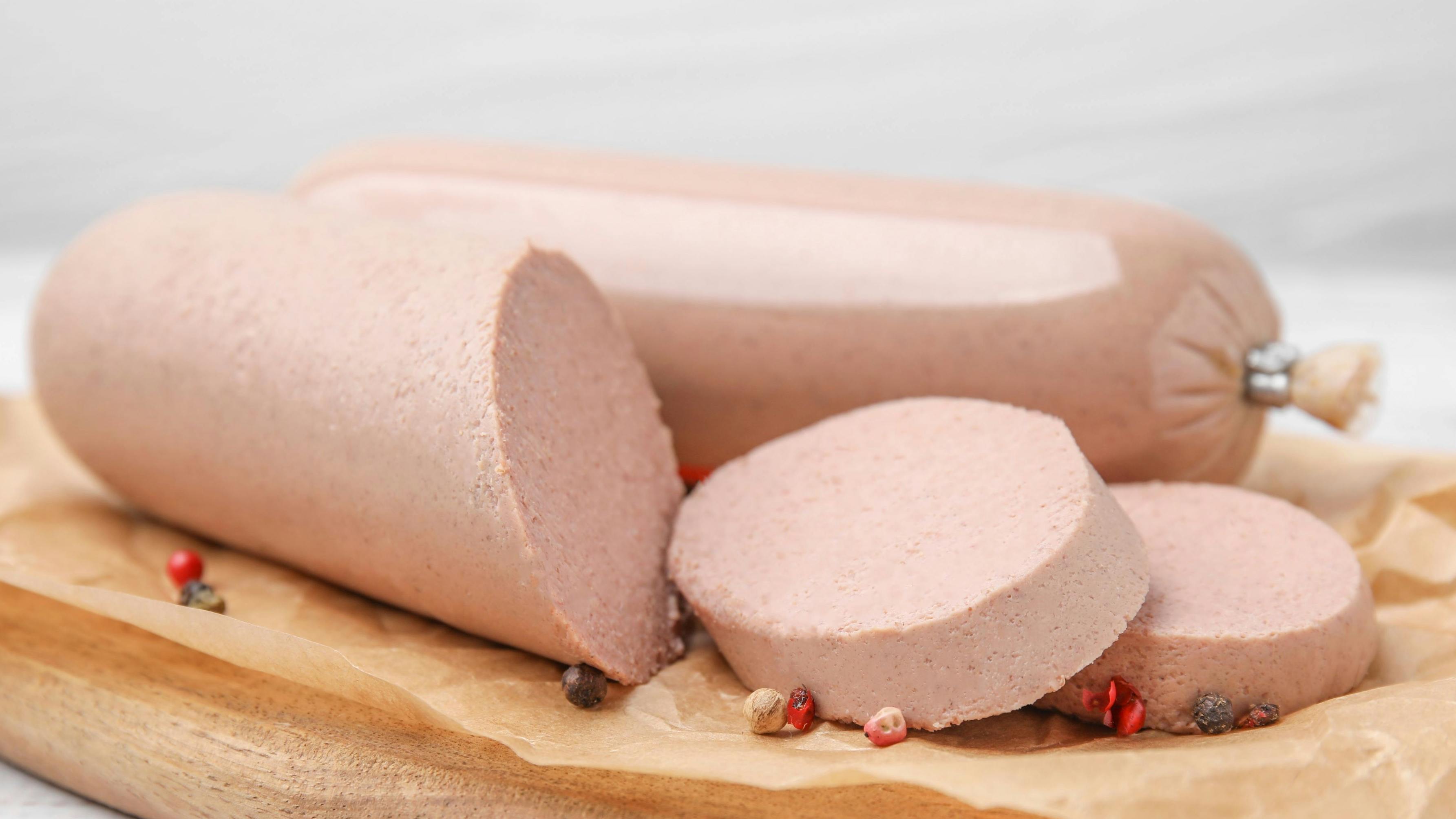 Board with delicious liver sausage on white wooden table, closeup
