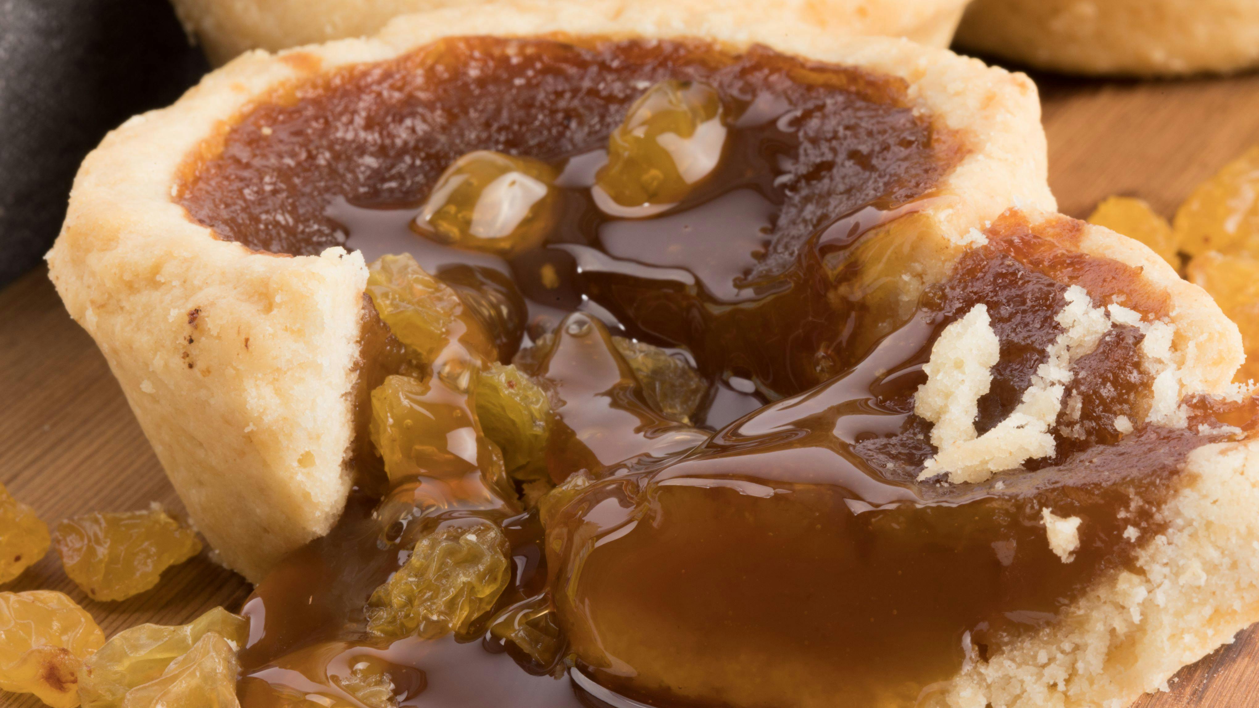 a butter tart on a wooden board showing the sweet filling and raisins flowing onto the board