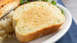 thick slice of garlic toast, part of a seafood entree, in a restaurant or kitchen setting thick slice of garlic toast, part of a seafood entree, in a restaurant or kitchen setting