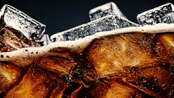 Cola with Ice. Close up of the ice cubes in cola water. Texture of carbonate drink with bubbles in glass.