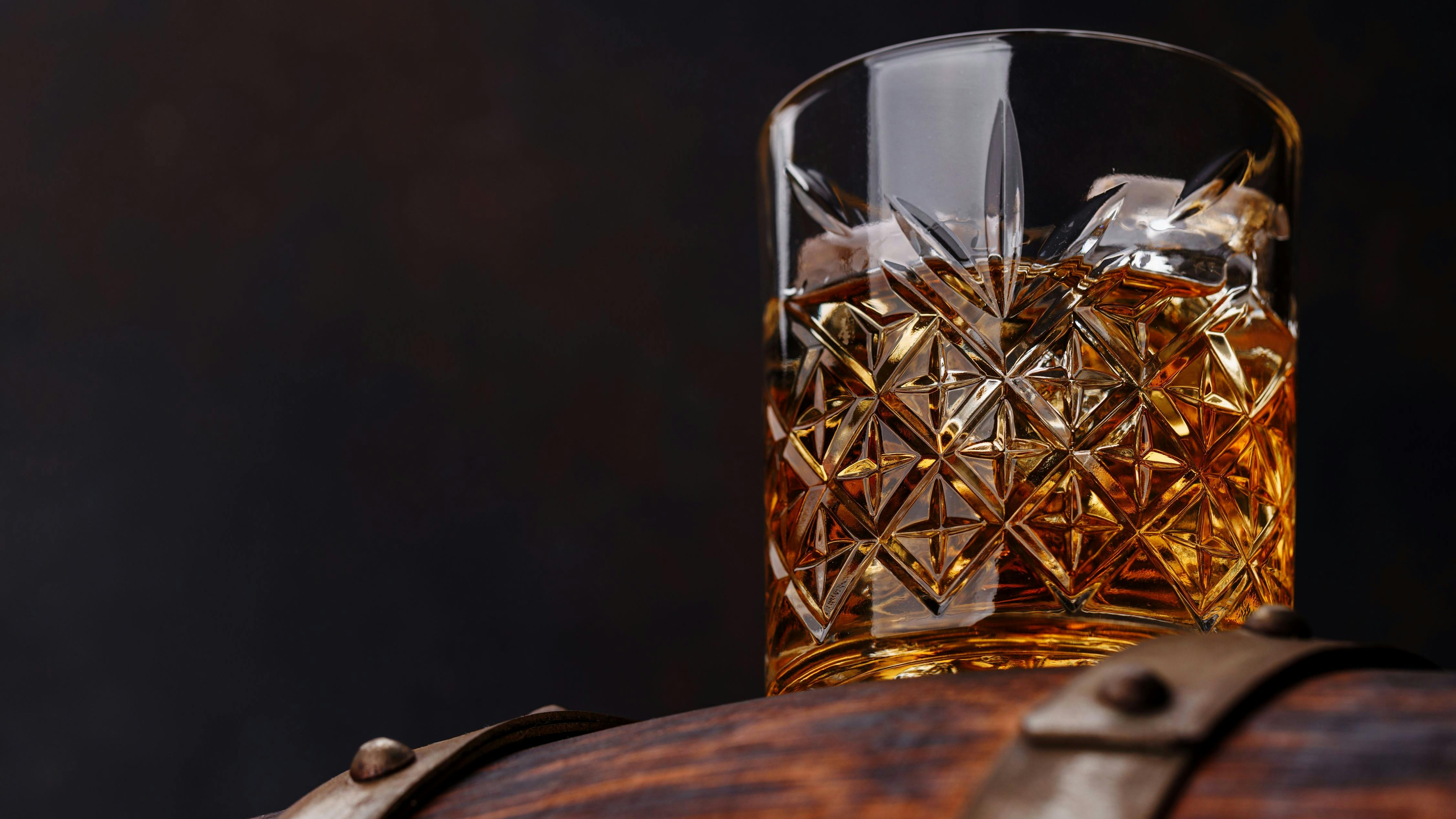 Whiskey glass with ice on a rustic barrel, a classic sip.