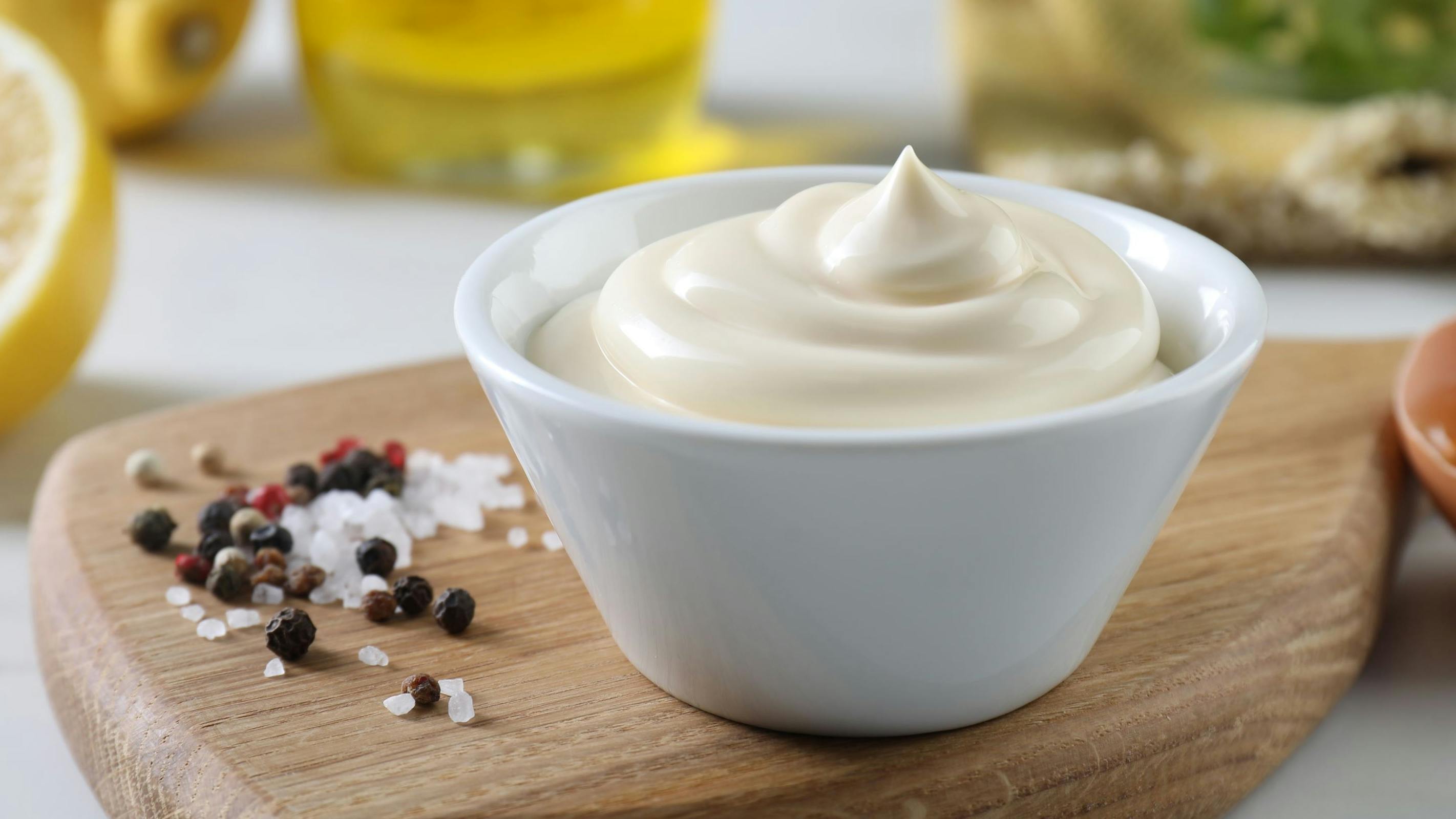 Tasty mayonnaise sauce in bowl, ingredients and spices on white table, closeup