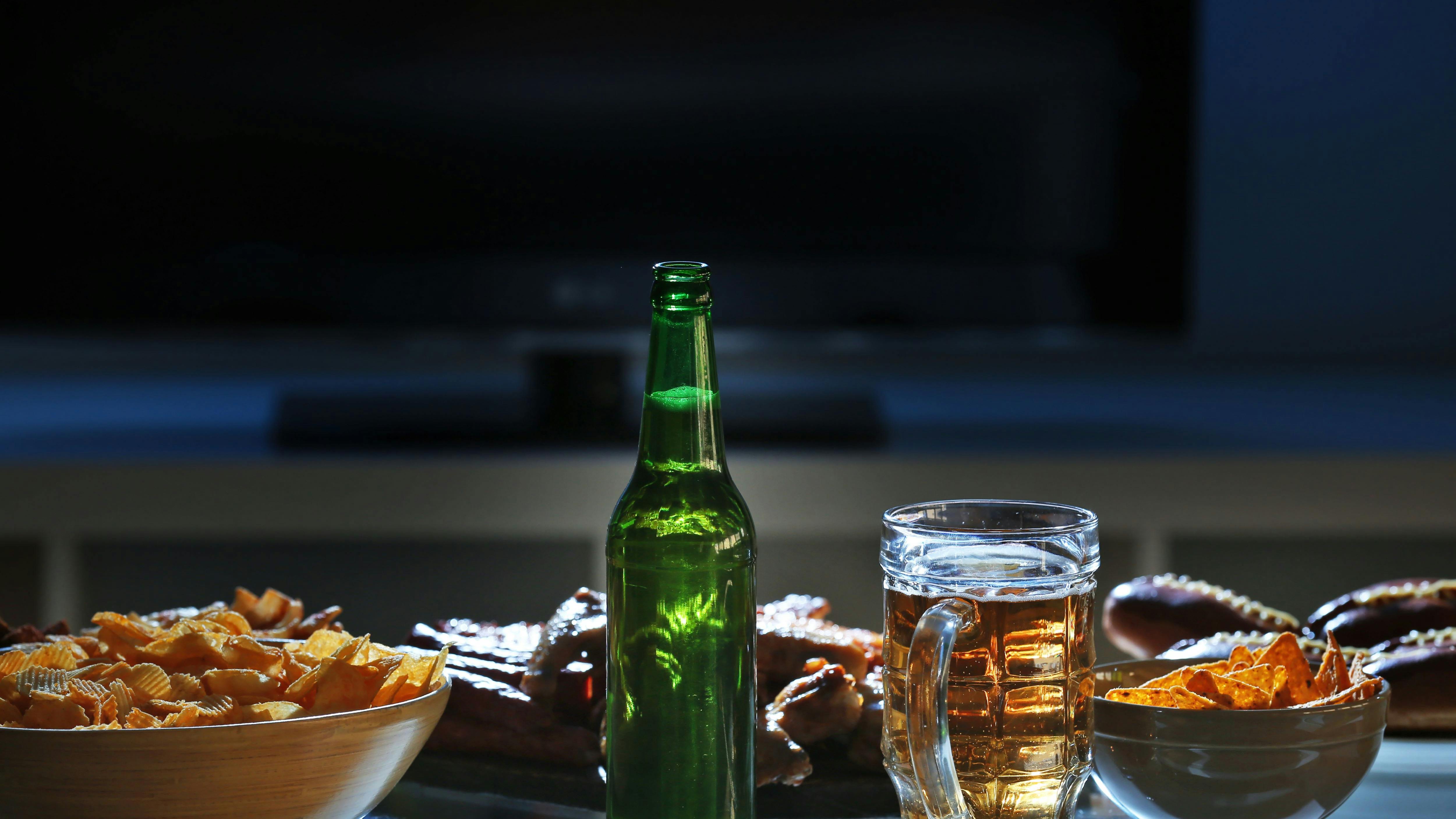 Tasty snacks and beer on kitchen table against blurred background