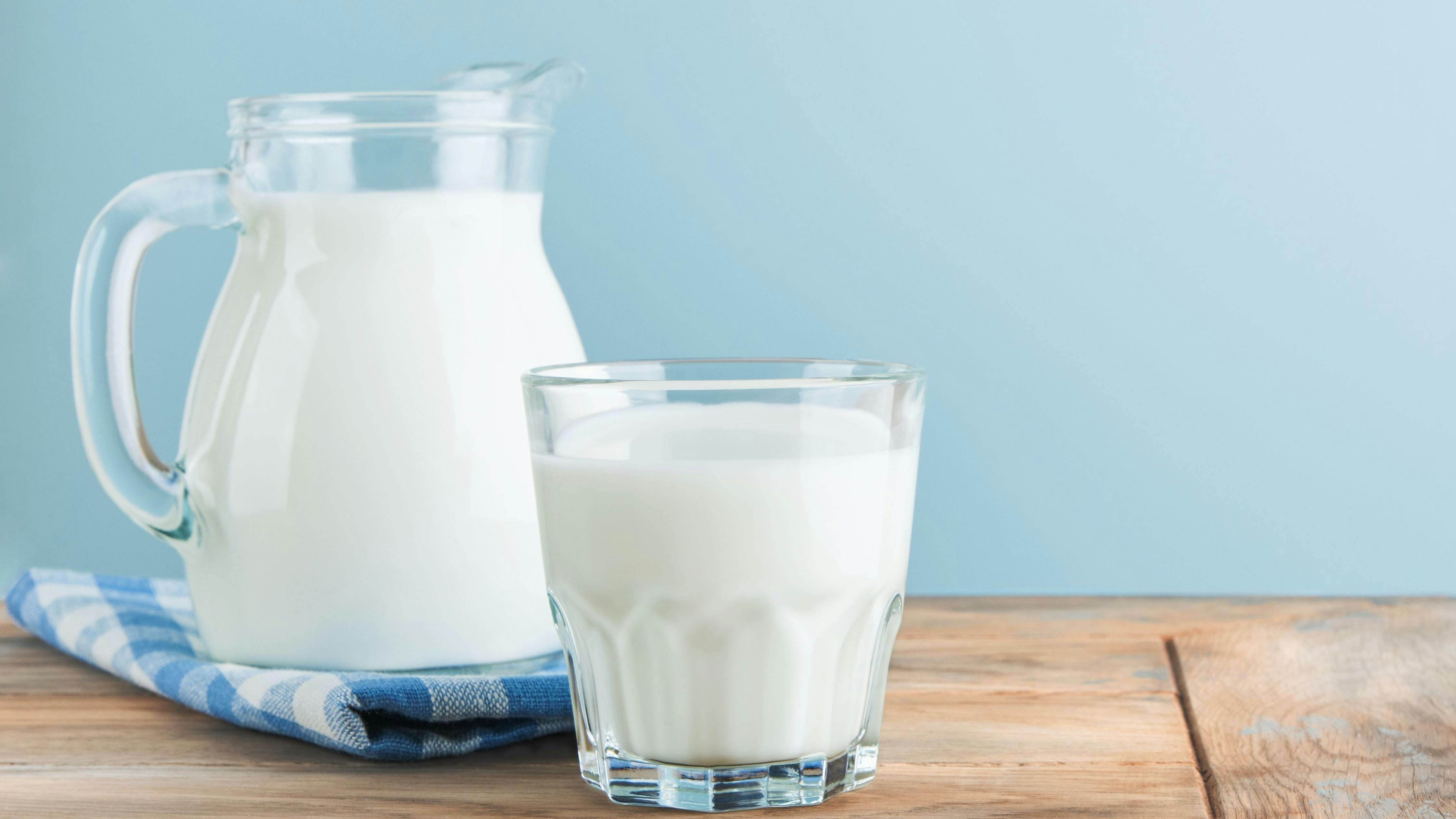 Milk in jug and glass on wooden table and blue background.