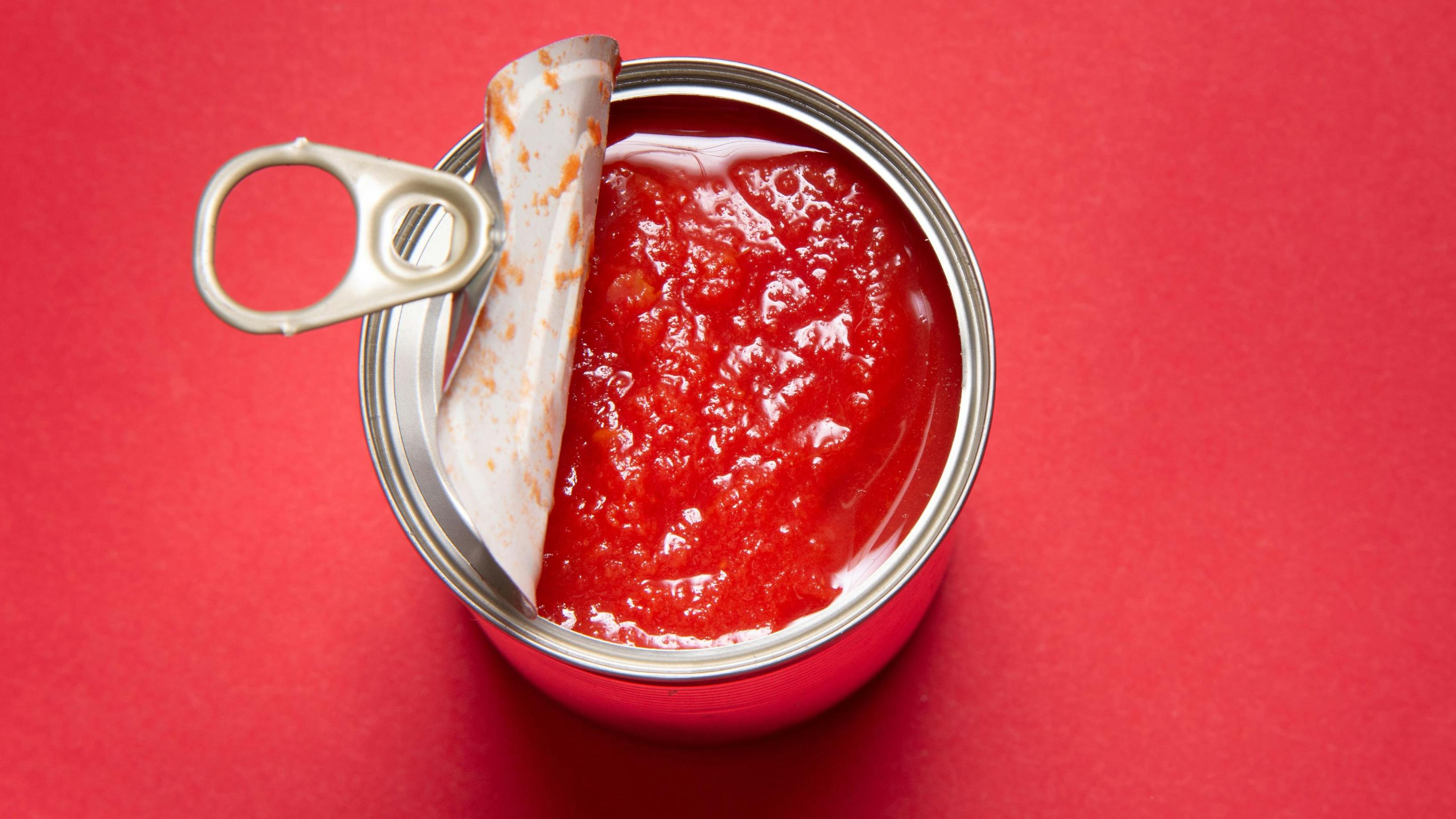 Opened tin can with canned tomatoes, on red background