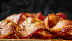Closeup photo of a pile of freshly cooked hot crispy bacon resting on a wood cutting board Closeup photo of a pile of freshly cooked hot crispy bacon resting on a wood cutting board