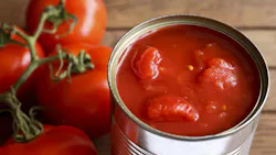Open tin of chopped tomatoes with whole fresh unfocused tomatoes behind. Wood surface.