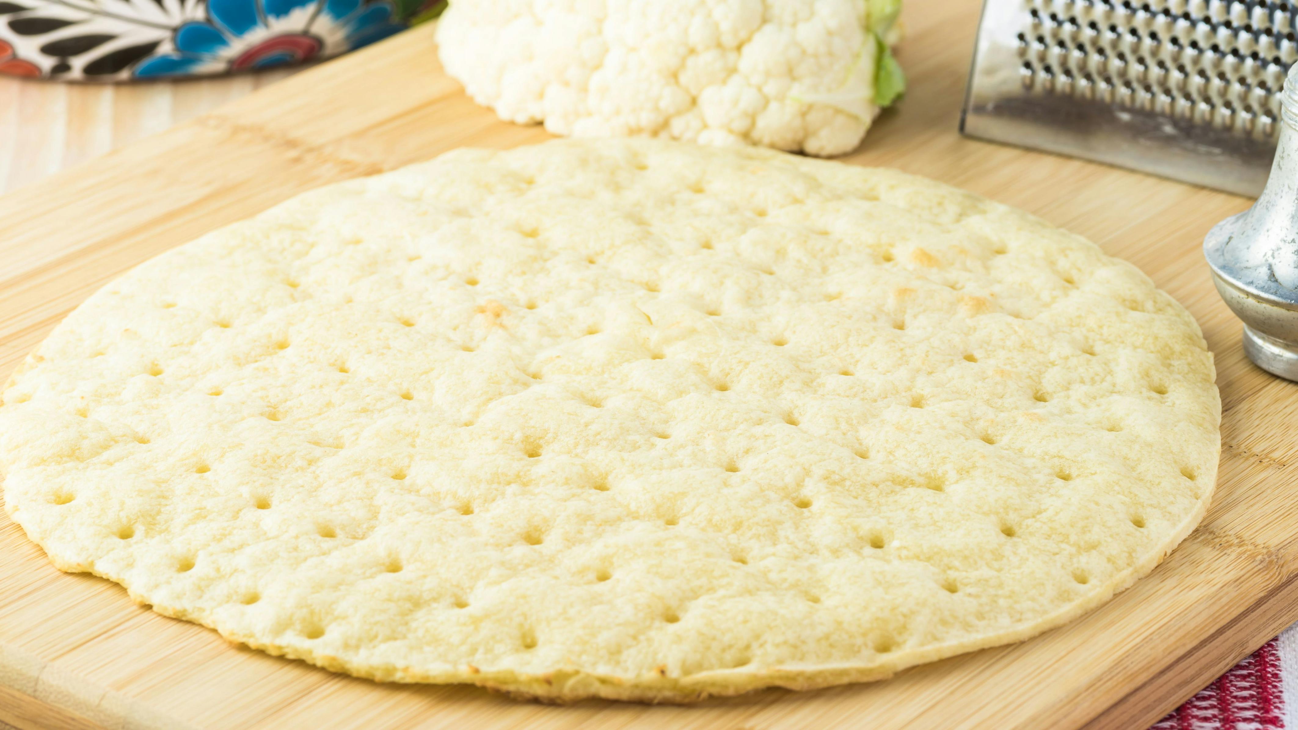 Close up of cauliflower pizza crust on a cutting board
