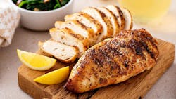 Grilled chicken breast with spice rub and lemon on a cutting board, sliced and whole Grilled chicken breast with spice rub and lemon on a cutting board, sliced and whole