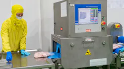 worker stands in PPE at conveying line with X-ray and metal detection equipment in a meat processing plant
