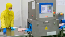 worker stands in PPE at conveying line with X-ray and metal detection equipment in a meat processing plant
